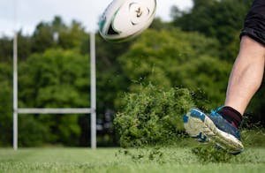 Close-up action shot of a rugby player kicking a ball on a lush green field in Galway, Ireland.