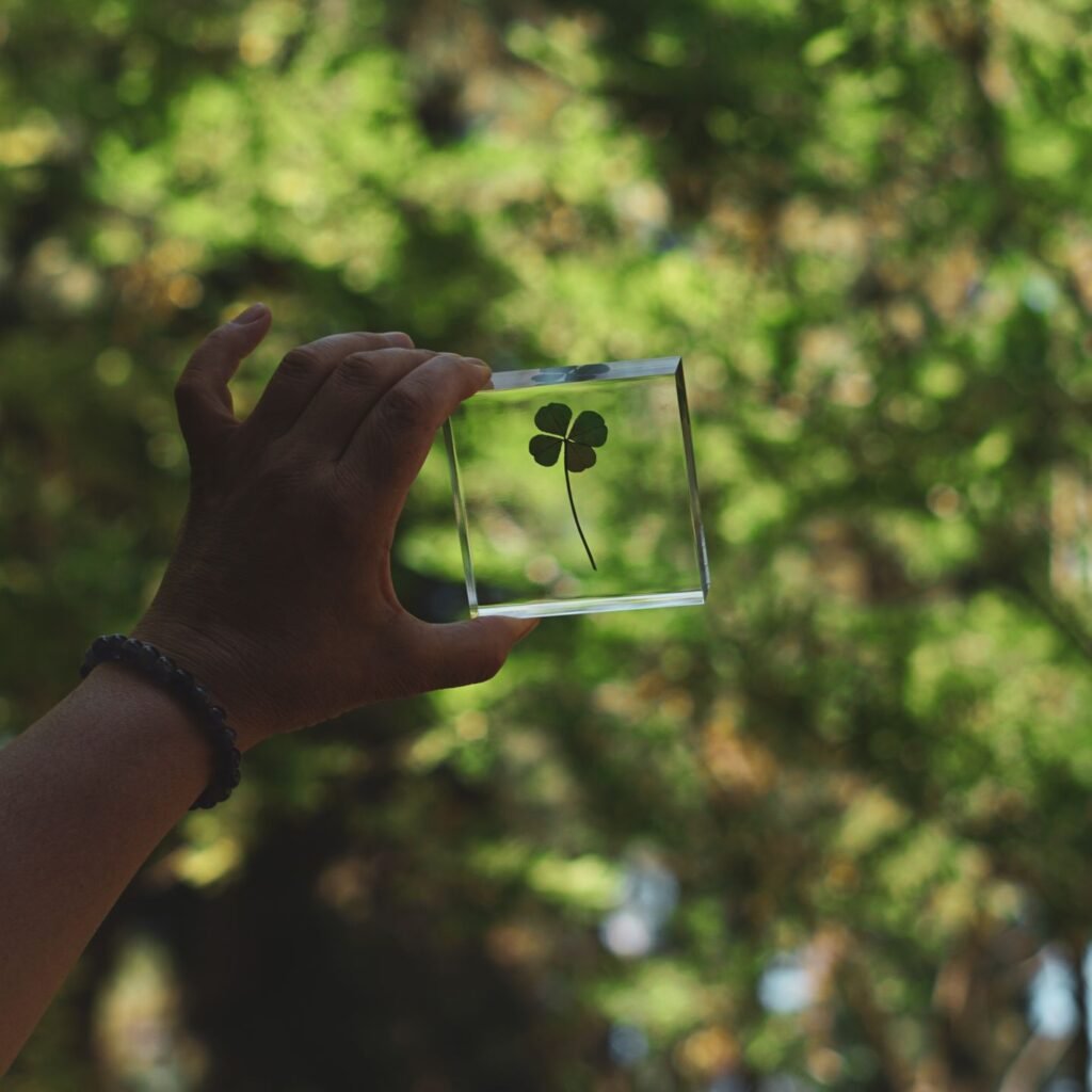 A hand holds a four-leaf clover encapsulated in a glass frame against a lush green background.